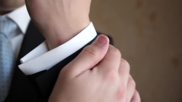 Man in blue tie and black jacket straightens sleeve of a white shirt. — Stock Video