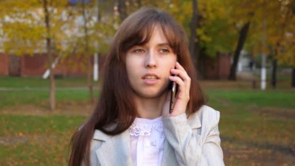 Bella donna che parla su smartphone e sorride. ragazza sta parlando al telefono cellulare e passeggiando nel parco della città la sera — Video Stock