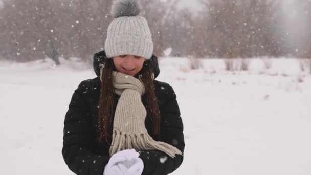 美丽的女孩做雪球和微笑。女孩走在冬季公园在降雪. — 图库视频影像