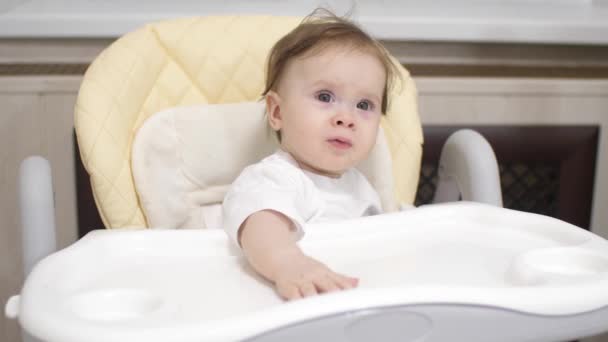 Pequeño bebé está sentado detrás de la silla alta en la cocina y sonriendo — Vídeo de stock