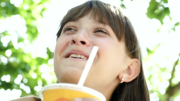Mädchen im Teenager-Alter im Park trinkt einen Cocktail aus Stroh und lächelt. Nahaufnahme. — Stockvideo
