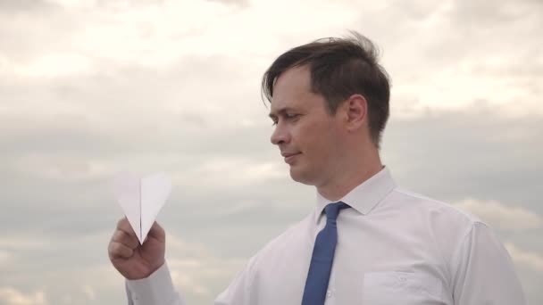 Hombre de negocios en camisa blanca y corbata azul está jugando con el avión volador de papel contra el cielo . — Vídeos de Stock