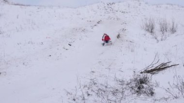 Çocuk atlı kızak ve gülüyor karda tepeden aşağı kayıyor. Kar kız yüzüne uçuyor. Parkta çocuklar Noel tatili. Ağır çekim