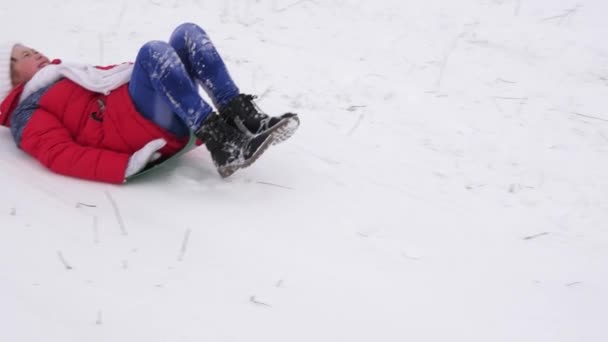 Menina escorrega na neve da colina no inverno. Criança brincando no parque de inverno durante as férias de Natal. Movimento lento — Vídeo de Stock