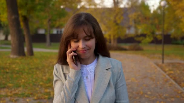 Telefono cellulare a piedi attraverso il parco autunnale e sorridente — Video Stock