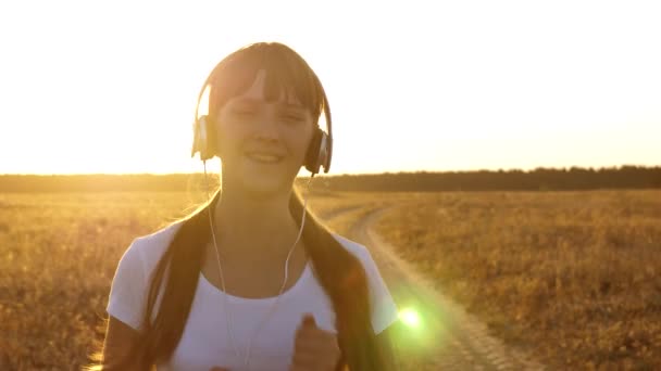 Niña está entrenando al atardecer y escuchando música. chica deportiva en los auriculares se dedica a trotar — Vídeos de Stock