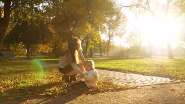 Mãe caminha com a criança no parque de outono ao pôr do sol. bebê está sentado no gramado, mãe cria bebê da grama . — Vídeo de Stock