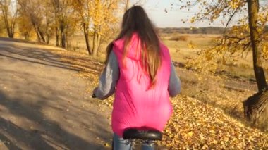 pembe ceket binicilik bisiklet, direksiyon simidi elleriyle sonbahar yolda tutan kız. Ağır çekim.