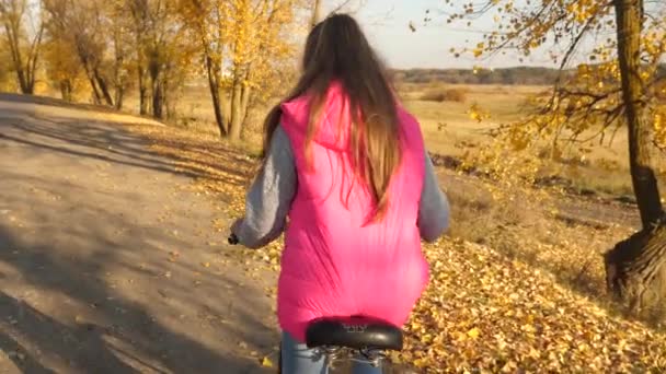 Menina de jaqueta rosa andar de bicicleta, segurando o volante com as mãos na estrada de outono. Movimento lento . — Vídeo de Stock