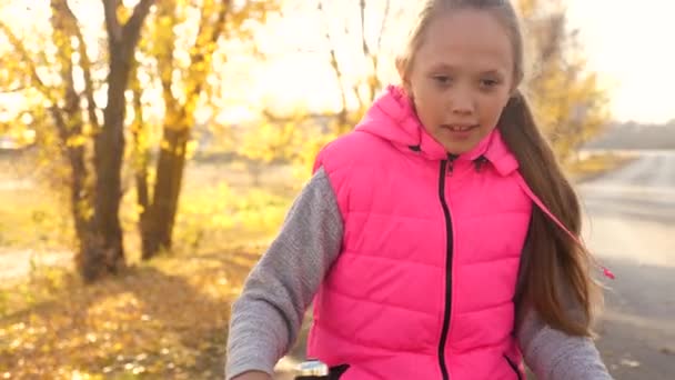 Bela menina adolescente monta bicicleta na estrada e ri. menina com cabelos longos e em bicicleta de equitação jaqueta rosa no parque de outono . — Vídeo de Stock