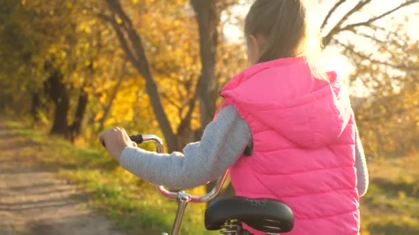 Meisje gaat op weg en rollen fiets. Wandelen in het park in de herfst. — Stockvideo