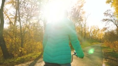 Kız sarı ağaç arka plan sonbahar Park'ta bir asfalt yolda bisiklet sürmek