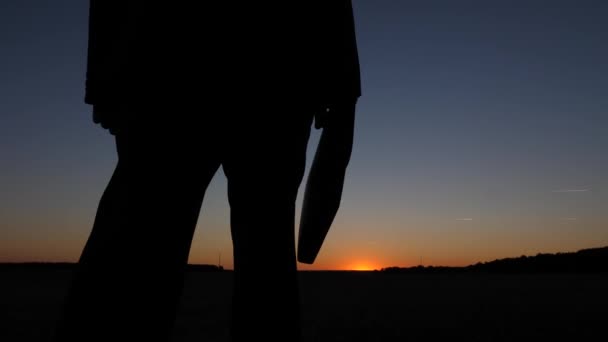Silhouet van zakenman met werkmap lopen bij zonsondergang, tegen blauwe hemel. Close-up — Stockvideo
