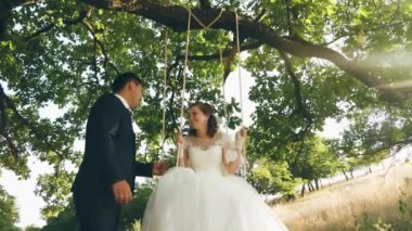 Mutlu genç çifte gelin ve damat gelinlik parkta salıncak üzerinde sallanan. Yaz orman ve birkaç içinde sevgi bir meşe dalı salıncağa. yakın çekim