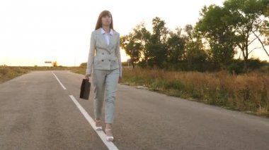 iş kadını siyah bir evrak çantası ile yürür ışık takım elbiseli ve beyaz yüksek topuklu ayakkabılar yürümek işaretleri ile asfalt cepheden görüntülemek