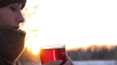 Kız bir kış parkta sıcak çay günbatımında içecekler..