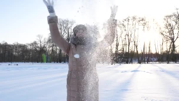 Mladá dívka vyvolá sníh v zimě park a úsměvy. Vánoční svátky. Zpomalený pohyb — Stock video