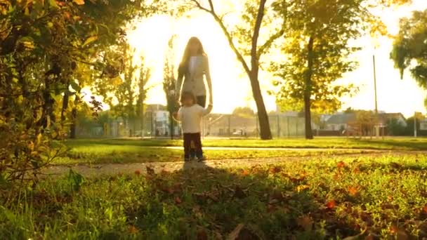 Mamma går med barn i höst park vid solnedgången. barn promenader längs sökvägen i vackra solstrålarna — Stockvideo