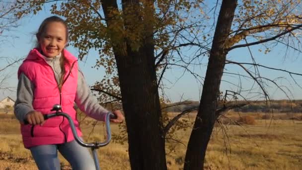 Fille heureuse en veste rose promenades vélo dans le parc d'automne. mains de fille tenir le guidon plié . — Video