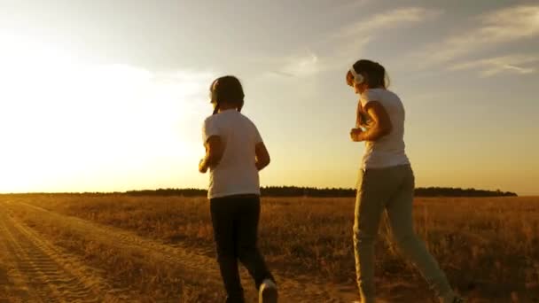 Meninas adolescentes em fones de ouvido musicais que praticam esportes no campo. meninas estão praticando jogging ao pôr do sol e ouvir música . — Vídeo de Stock