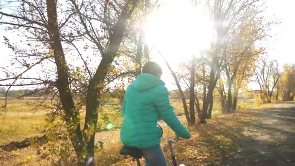 Fiatal lány lovaglás kerékpár út egy őszi út szélén. Lassú mozgás — Stock videók