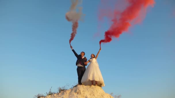 Šťastná nevěsta a ženich mává barevné růžový kouř proti modré obloze a směje se. Líbánky. Romantiku. Vztah mezi mužem a ženou — Stock video