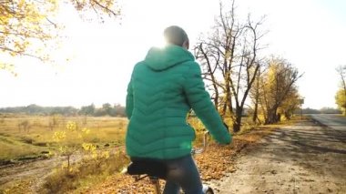 Kız güneşin parlak ışık sonbahar yaprakları üzerinde bisiklet sürmek