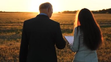 Evrak Çantası'nı el ile ciddi elbiseli yaşlı bir işadamı çalışma planı pozitif üzerinde parlak güneşte akşam şirket genç iş kadını için verir