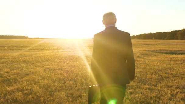 Літній бізнесмен у серйозному костюмі з портфелем в руці ходить по дорозі ввечері в дзеркалі встановлення сонця — стокове відео