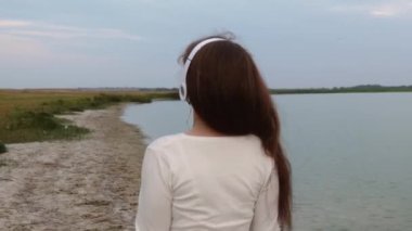 Kulaklık kız mutlu plaj boyunca yürür ve dans ederken gülüyor
