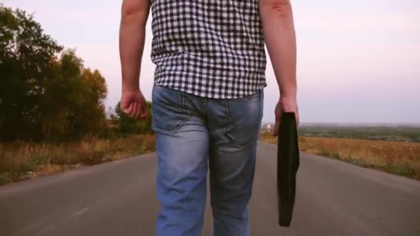 Mannelijke zakenman in plaid shirt is een wandeling langs een asfaltweg met zwarte aktetas met documenten in de hand. Close-up — Stockvideo