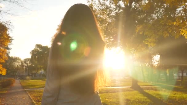 Mujer de negocios en traje de negocios camina en el parque en los rayos de la puesta del sol — Vídeos de Stock