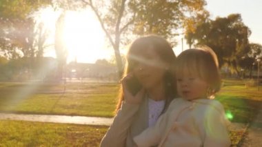 İş kadını iş takım küçük bebek ile smartphone üzerinde konuşmak ve gülümser ve gün batımı ışık sonbahar parkta yürüyüş