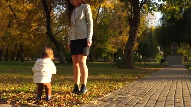 Business kvinna i kostym med lilla bebis promenader i höst park på kvällen sunset. Moderna upptagen mor promenader i kväll med barn efter jobbet. — Stockvideo