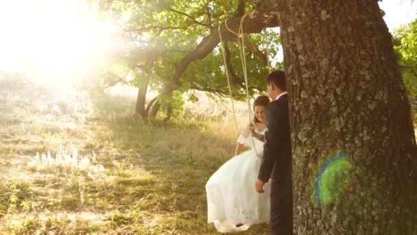 Bruid en bruidegom swing in zomer Park op schommel. touw schommel op een eiken tak in het bos — Stockvideo