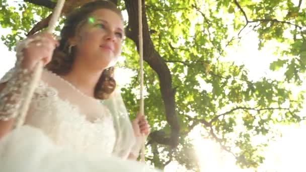 Счастливая невеста в белом платье, качающаяся на качелях в парке на ветке дуба. макро — стоковое видео