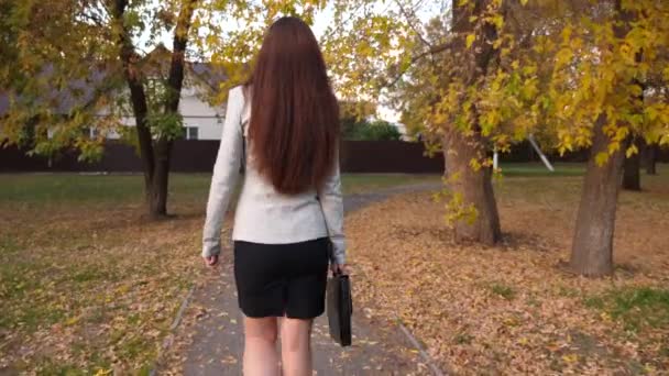 Geschäftsfrau in Rock und Jacke mit schwarzer Aktentasche in der Hand, die im herbstlichen Park entlang des Weges läuft. zurück — Stockvideo