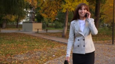 güzel iş kadın üstünde hareket eden telefon, Sonbahar Park yürüyüş ve gülümseyerek mutlu bir kadın söz