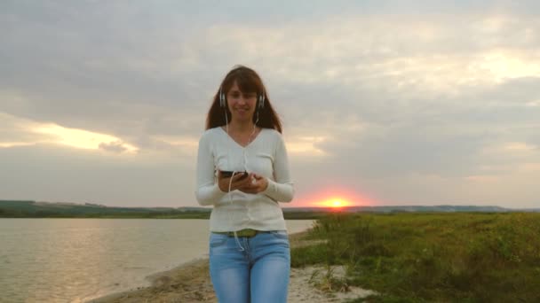 Красивая девушка в наушниках прогулки по пляжу с планшетом и видеоконференции онлайн — стоковое видео
