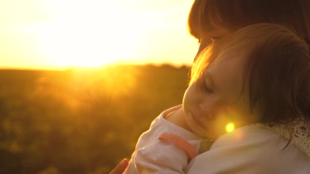Little girl is sleeping in arms of young mom in golden rays of sunset. Slow motion — Stock Video