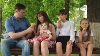 Anne ile çocuk parkı dondurma yeme ve gülerek bankta oturuyor. Mutlu bir aile