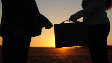 kadın adam için evrak çantası'nı geçer ve eller, güzel bir gün batımı fon karşı sallıyor. iş kadını ve işadamı anlaşma.