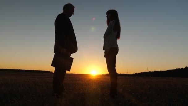 Silhouette affärsman och ung affärskvinna gjort affär, pass svart portfölj till varandra och skakar hand mot bakgrund av solnedgången mot den blå himlen — Stockvideo