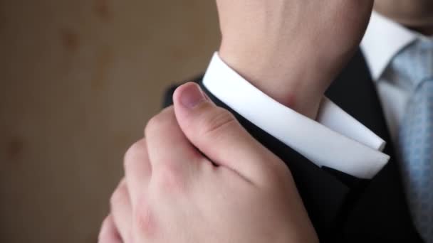Hombre con corbata azul y chaqueta negra endereza la manga de una camisa blanca. primer plano — Vídeo de stock