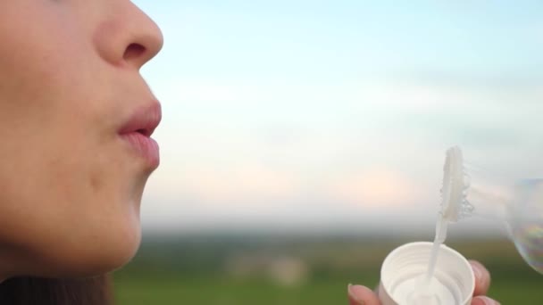 Young girl blowing transparent soap bubbles against the blue sky and laughing. Slow motion. — Stock Video