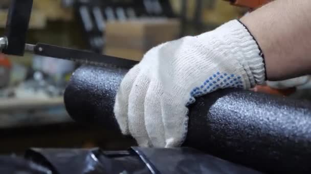 Schlosser in Schutzhandschuhen sägt schwarzes Rohr mit einer Bügelsäge ab. Der Mensch arbeitet in der Manufaktur. Nahaufnahme — Stockvideo