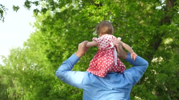 Днем тато несе маленькою дочкою на його плечі, Прогулянка в парку на лавці — стокове відео