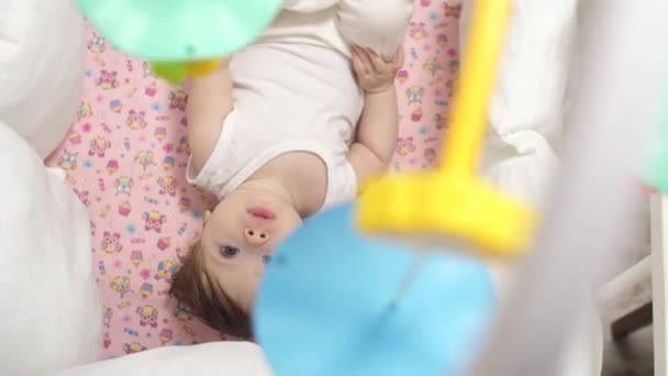 Маленька дитина лежить в колисці і дивиться на обертові іграшки . — стокове відео
