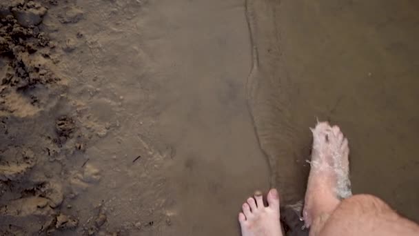 Mens voeten lopen blootsvoets langs de kust, opspattend waterdruppels in verschillende richtingen. Slow-motion. Close-up. — Stockvideo