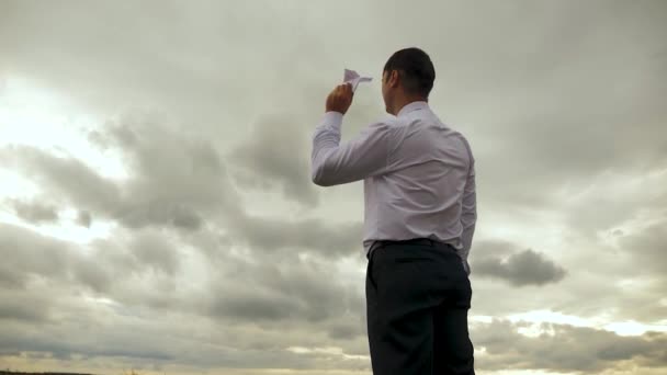 Podnikatel v bílé košili si hraje s papírem létající letadlo proti pozadí tmavé mraky. Zpomalený pohyb — Stock video